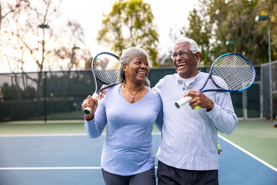 Photo of an older couple holding tennis rackets laughing together