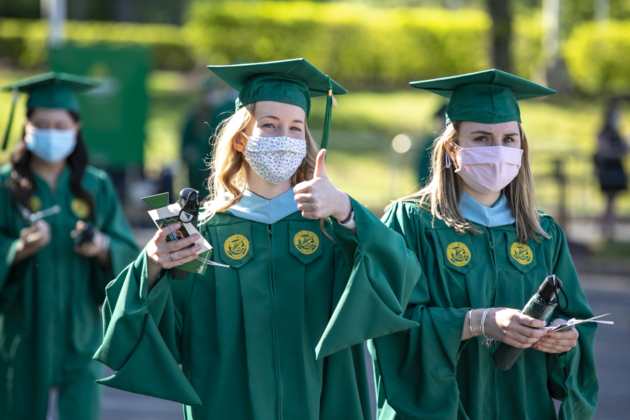 Recent alumni in graduation gowns, one giving a thumbs up