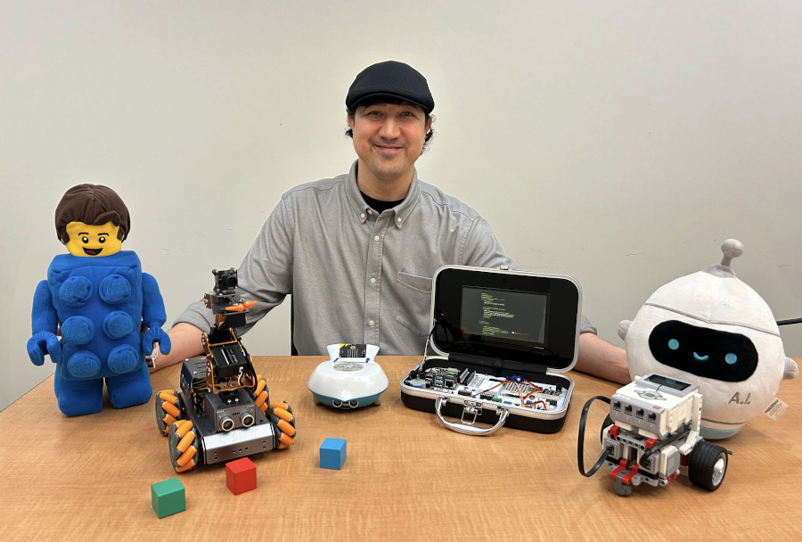 Erdogan Kaya sitting behind a desk with robotics- and AI-related toys and machines