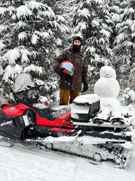 Brenden standing beside a snowmobile and a snowman