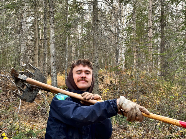 Brenden carrying tools over his shoulder through the forest
